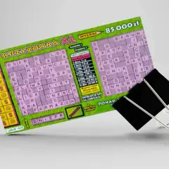 Zdrapka z krzyżówką XL z nagrodą 85 000 zł, przytrzymana przez czarny klips biurowy.