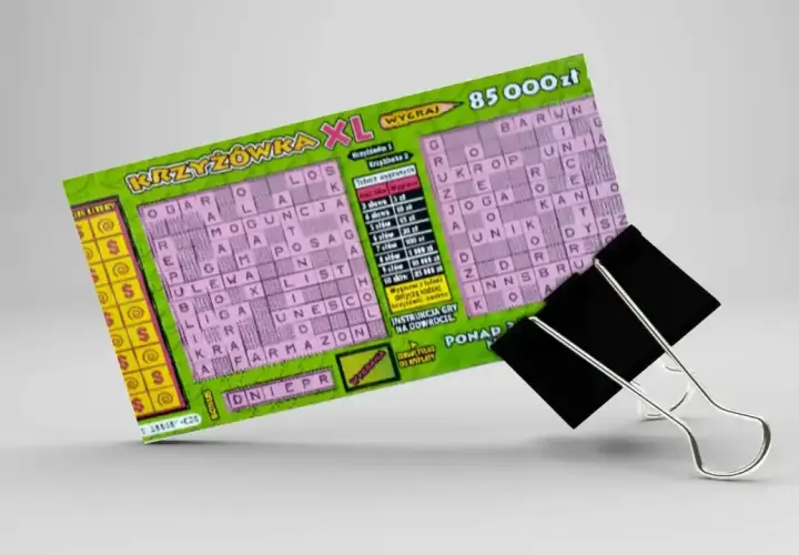 Zdrapka z krzyżówką XL z nagrodą 85 000 zł, przytrzymana przez czarny klips biurowy.
